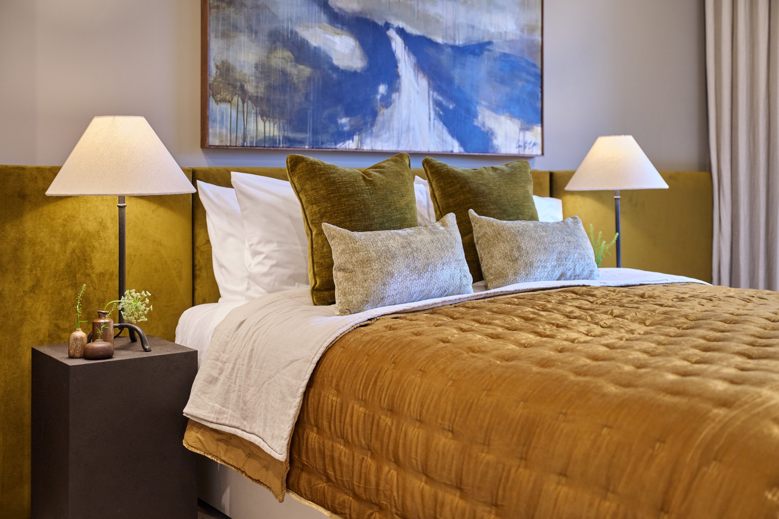 Ebury new apartment showing master bedroom showing double bed with gold bedspread and headboard, velvet cushions and wooden side tables with table lamps