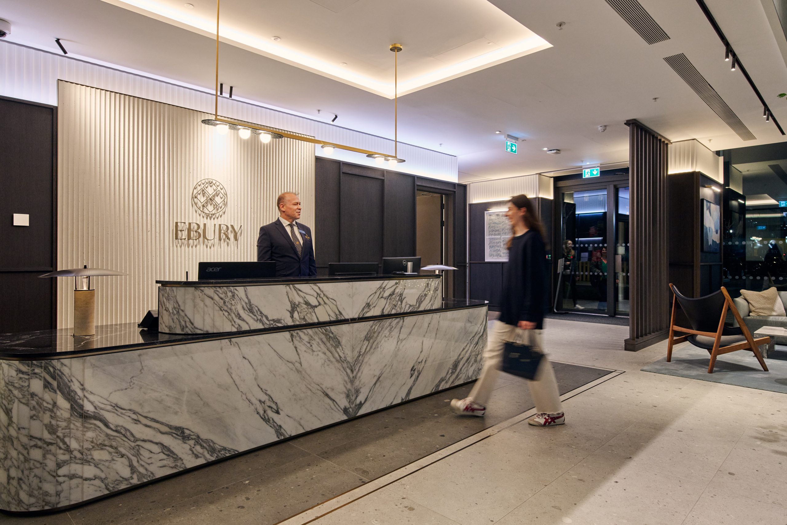 Stylish lady approaching marble fronted concierge desk with man behind desk waiting to greet her