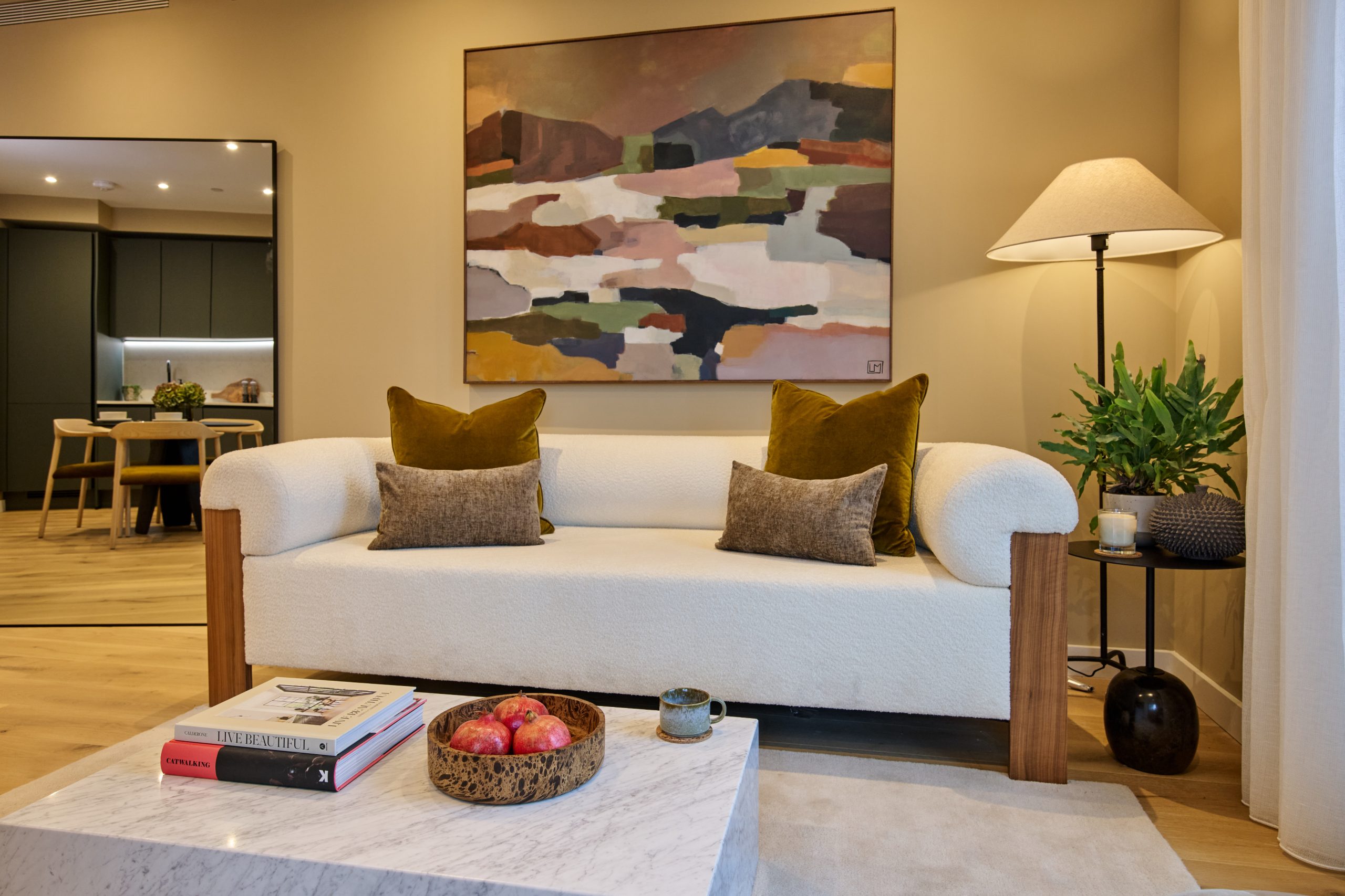 Apartment living area showing white sofa and square marble effect coffee table with large mirror in the background showing a reflection of the kitchen