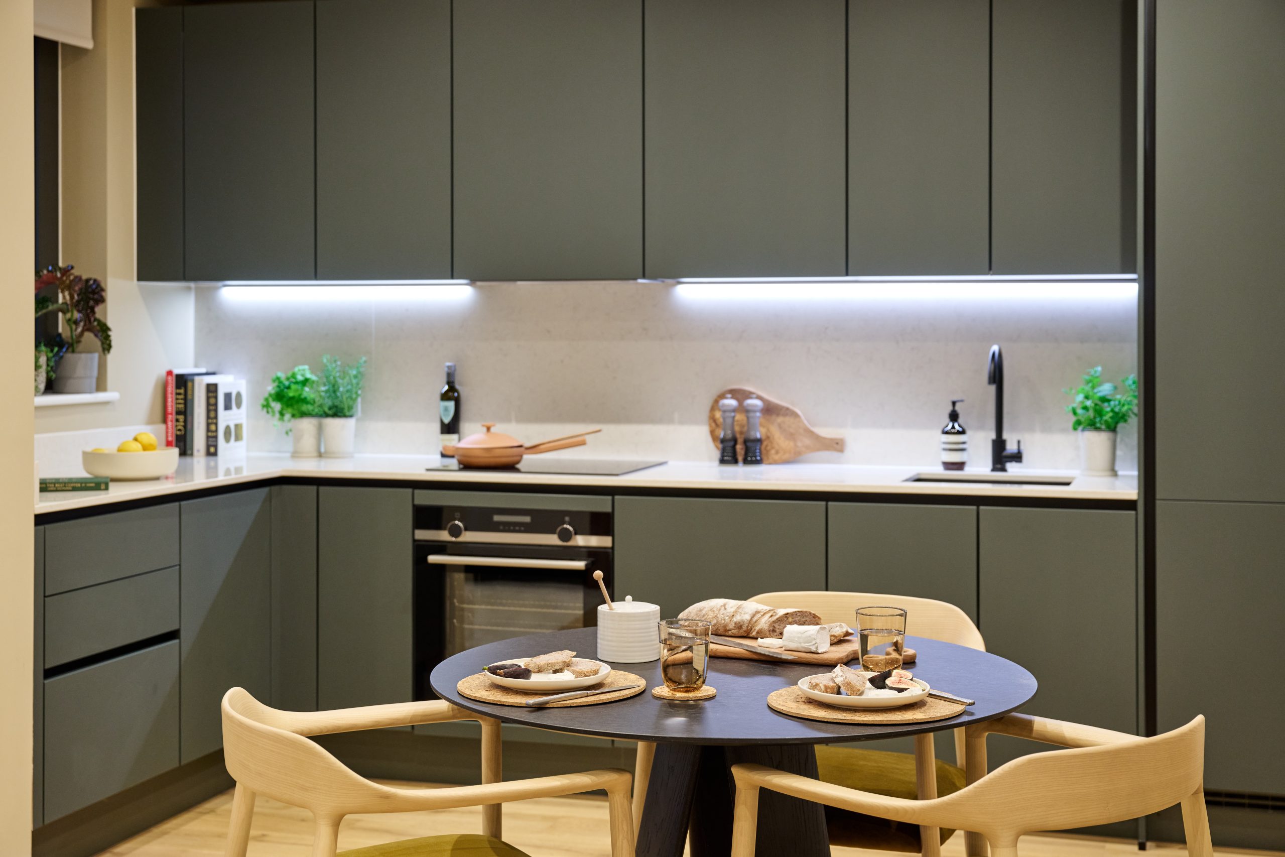 Kitchen area inside an Ebury apartment. Cupboards and kitchen surface areas including a tap, condiments and built-in oven are int he background, with a table and three chairs with dinner on the table in the foreground