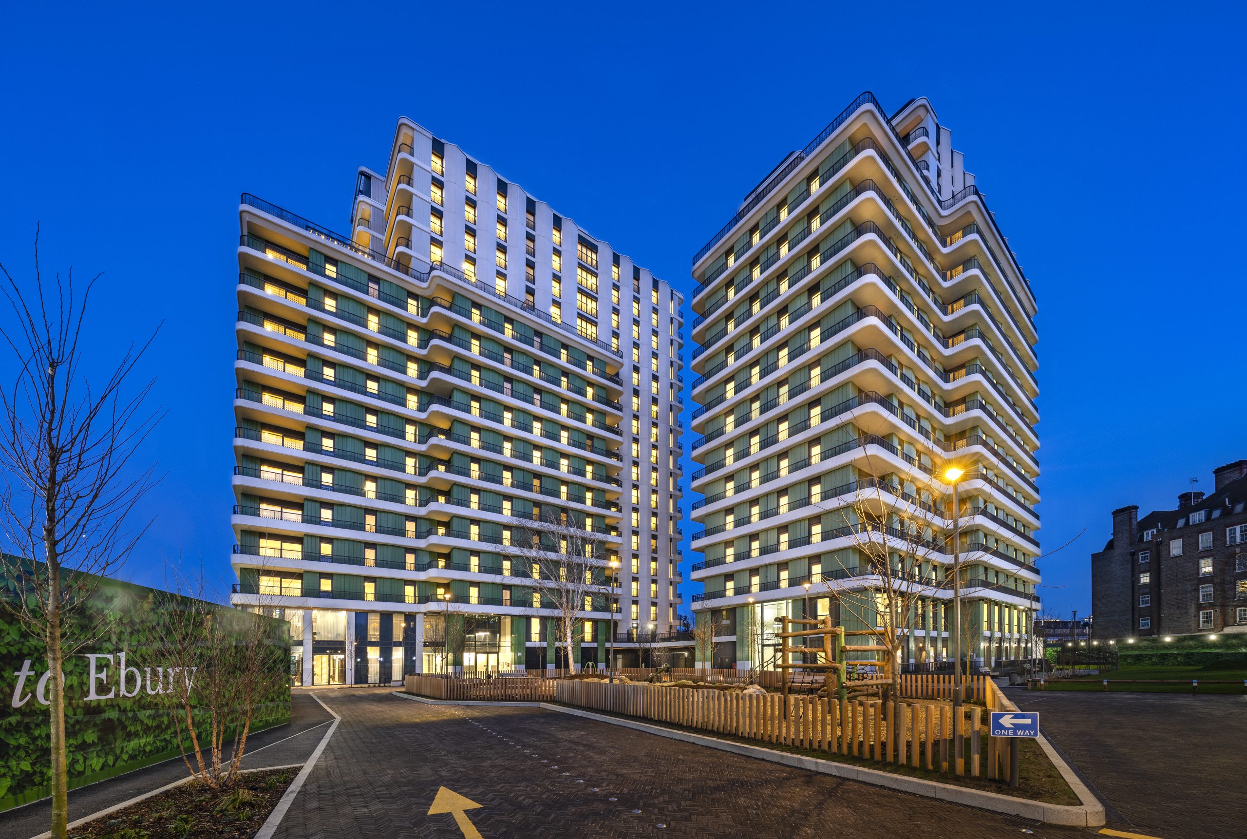 The multi award-winning Ebury development as viewed from the outside street in the evening. Two buildings feature with the lights on in all windows as well as the road leading towards them