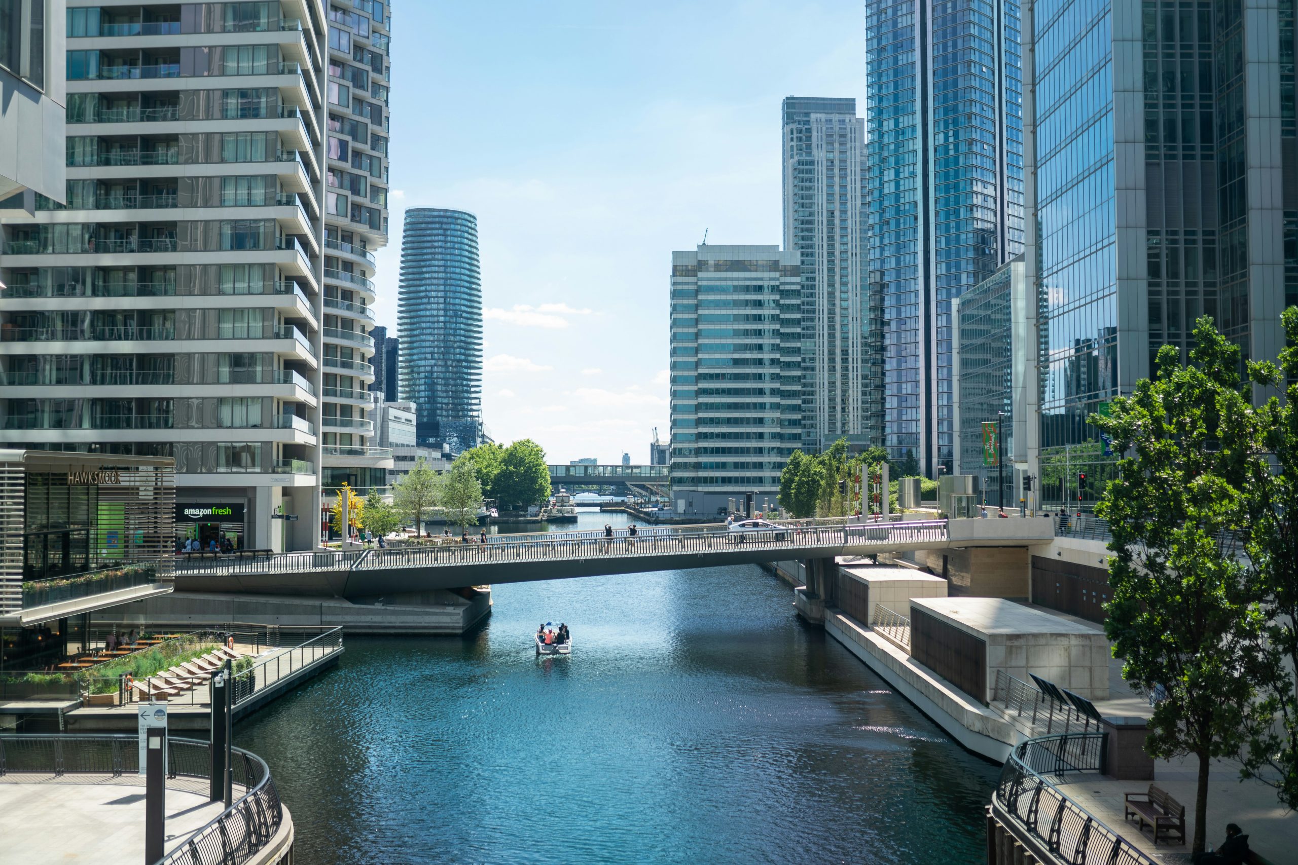 Waterside view of Canary Wharf featuring tall office buildings on either side and a bridge in the distance