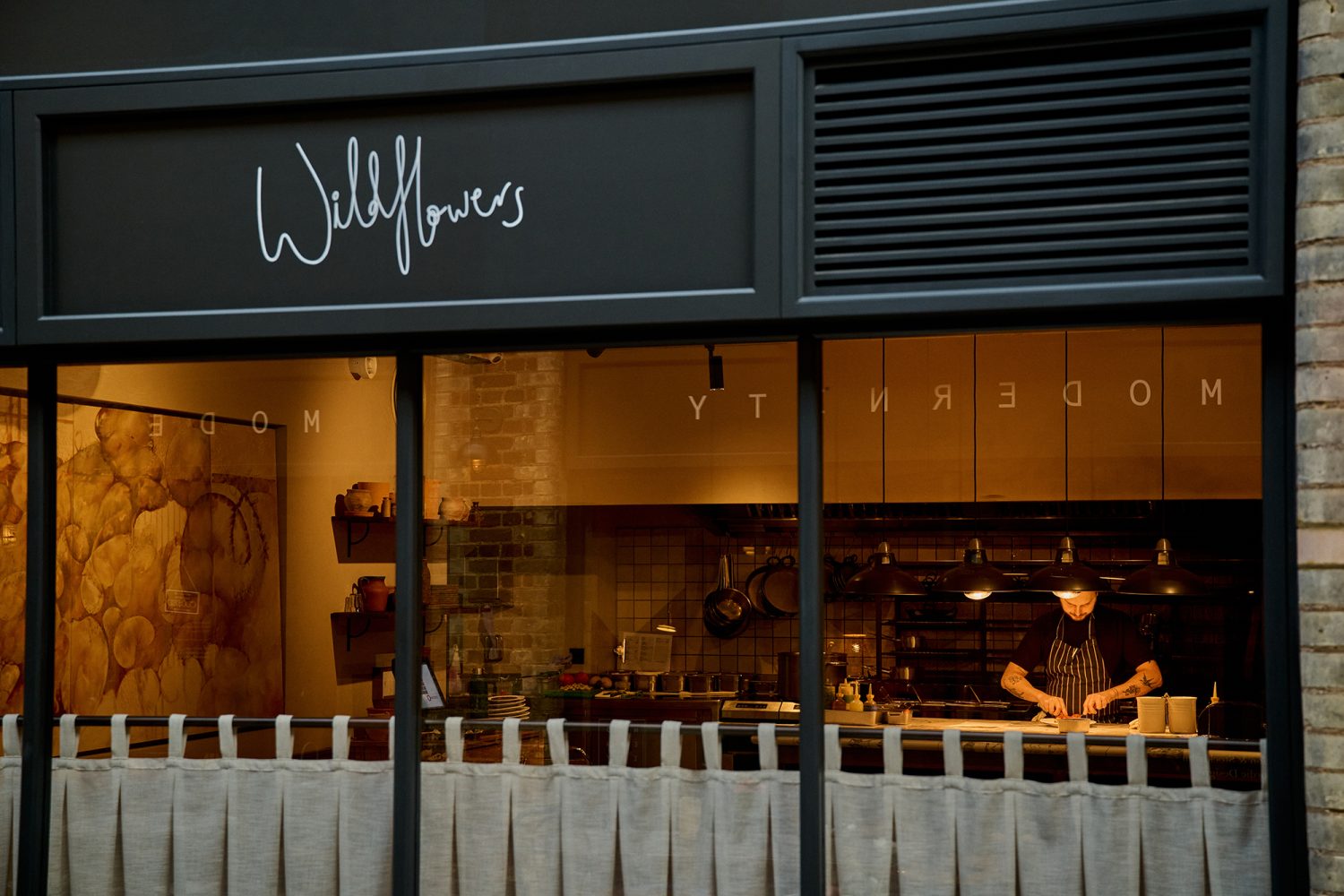 Close up view of the window of Wildflowers restaurant. Through the glass you can see the chef working in the kitchen in the background.