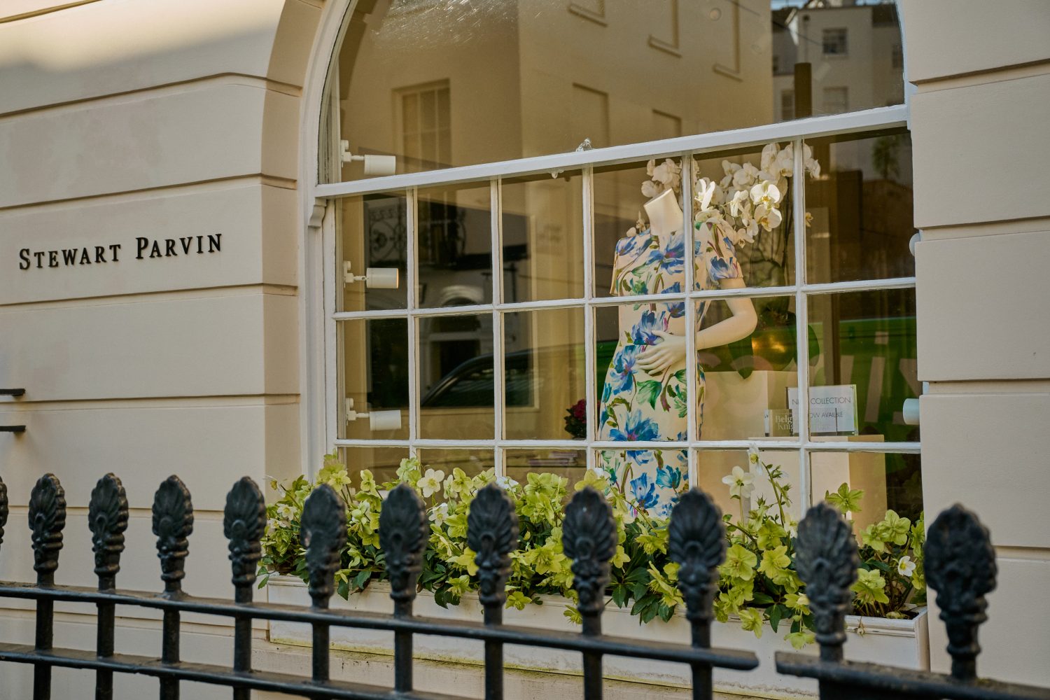 A close up view of a fashion store showing a mannequin in the window wearing a floral dress