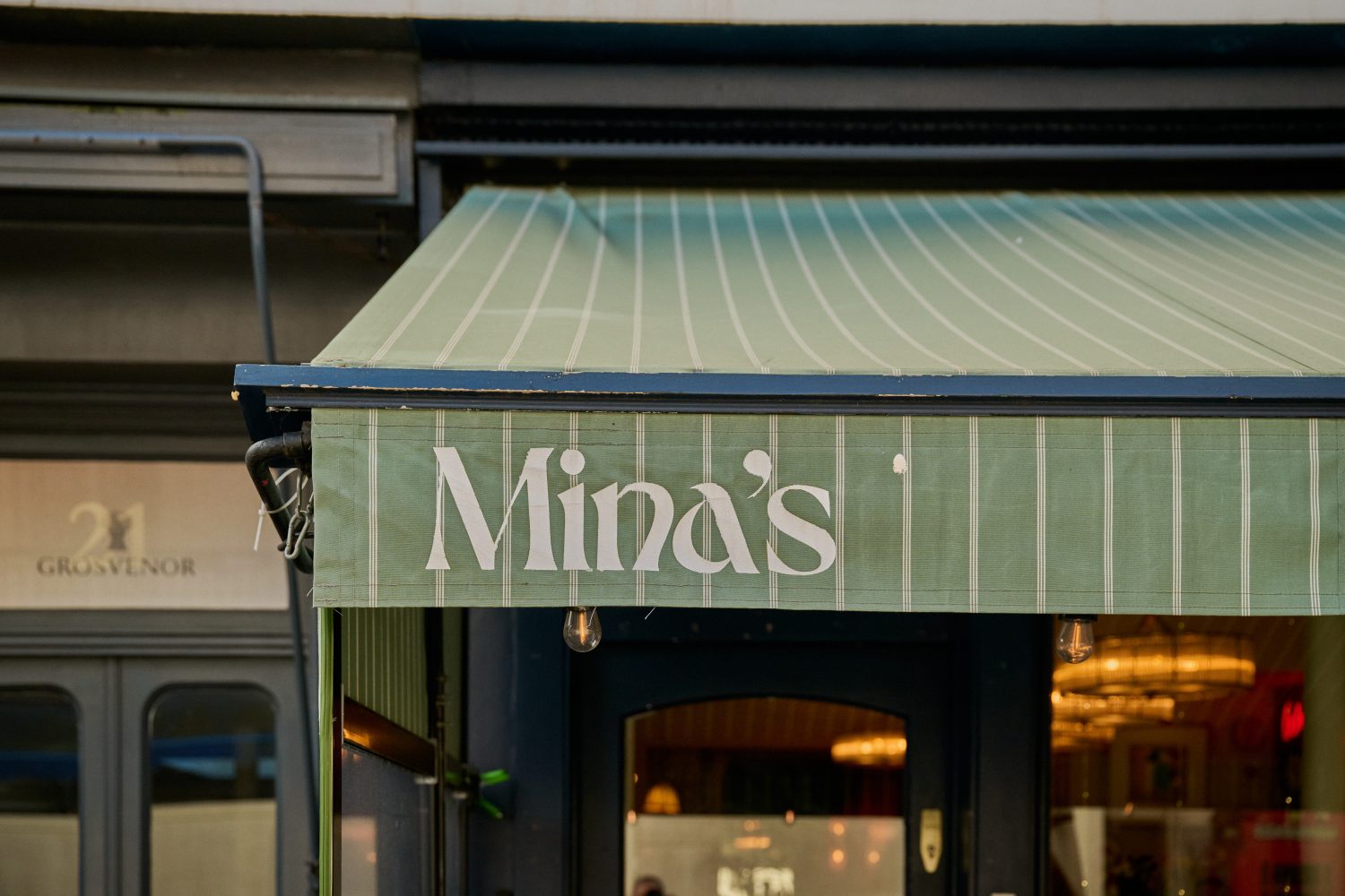 Close up view of the green awning of a restaurant with its name 'Mina' displayed