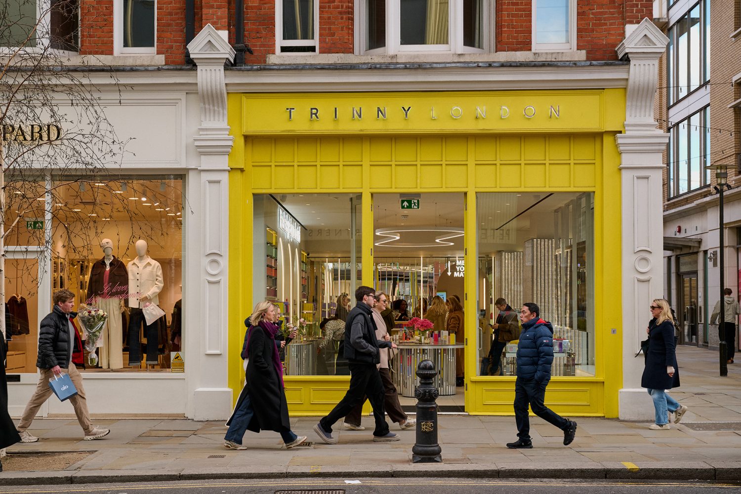 Bright yellow shop front for Trinny London beauty shop on King's Road with smartly dressed people walking past