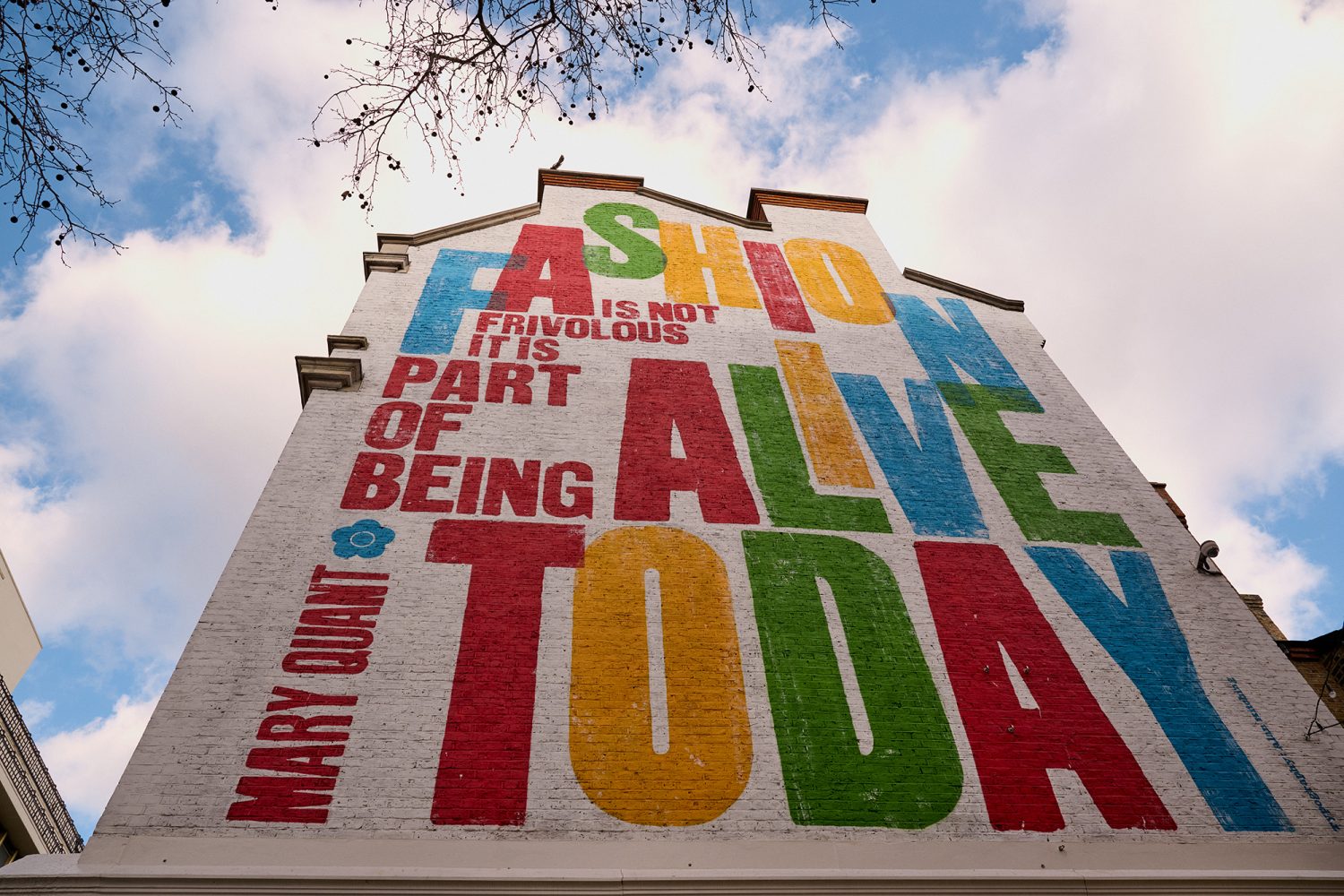 Close up of brightly painted lettering in green, red, yellow and blue on the side of a building, reading: 'Fashion Alive Today'