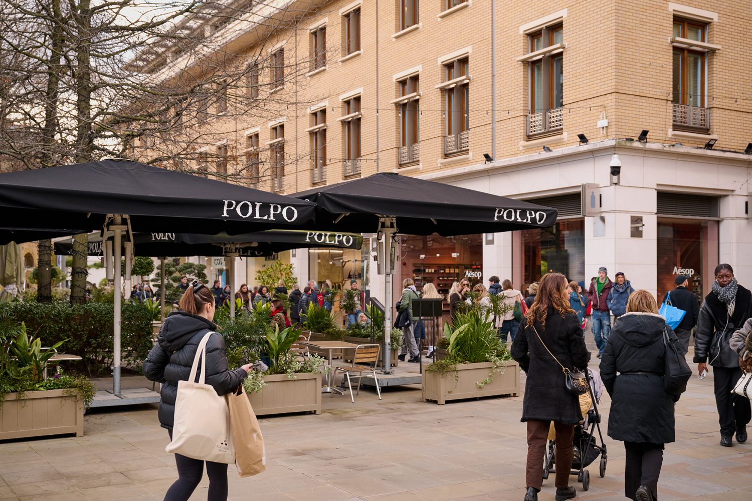 View across Duke of York Square showing shoppers and the entrance to Polpo restaurant showing outside seating covered by large black parasols