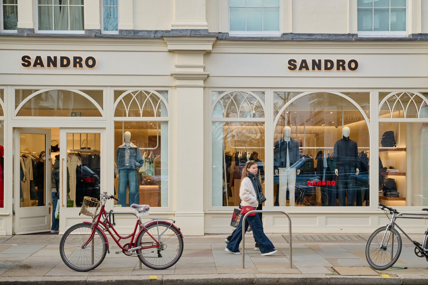 A lady walking past a fashion store on King's Road with two bicycles chained up outside