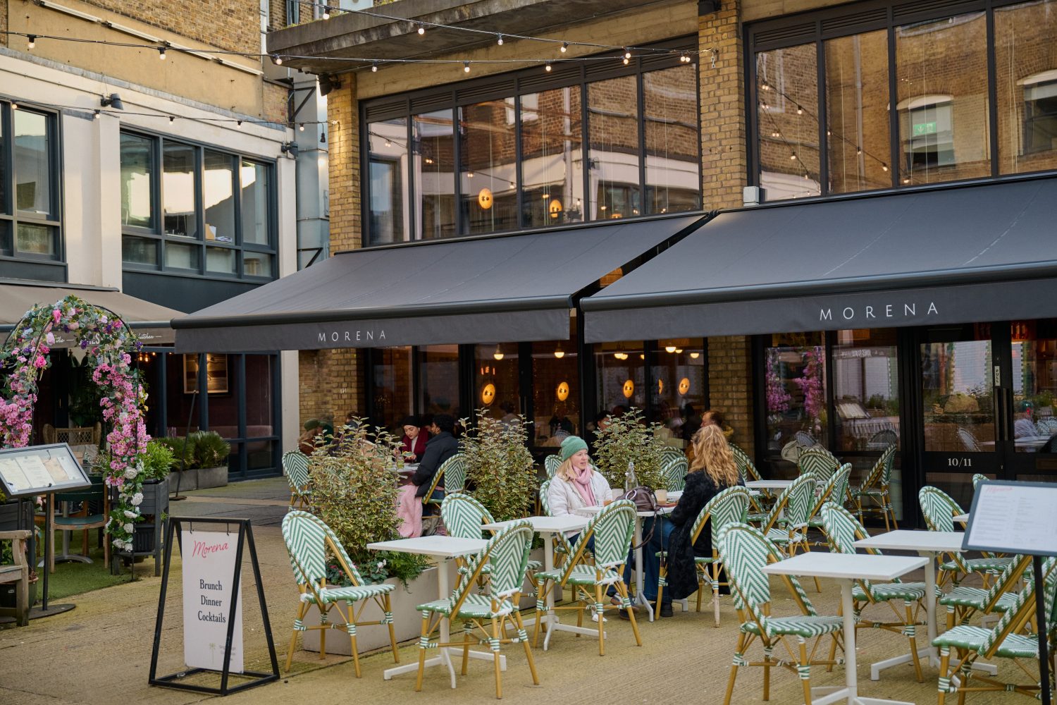 Two ladies enjoying a drink outside a restaurant on pale green coloured chairs and tables in a quiet London square