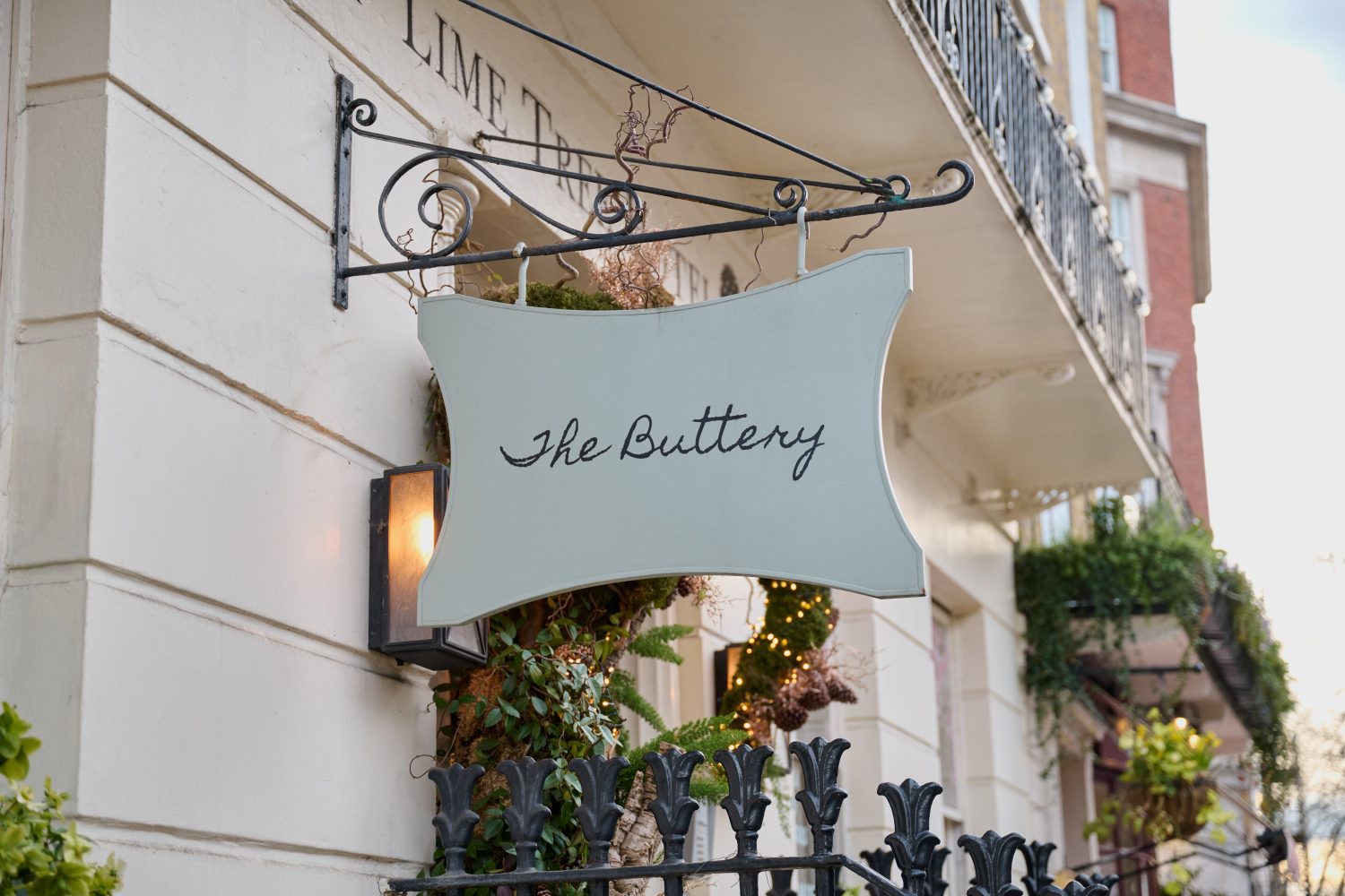 Close up view of an ornate sign outside a smart looking cream coloured stone building. The sign reads 'The Buttery'