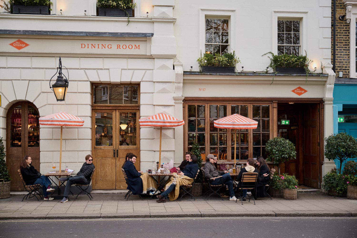 People seated at tables and chairs enjoying drinks outside The Orange Pub in Pimlico