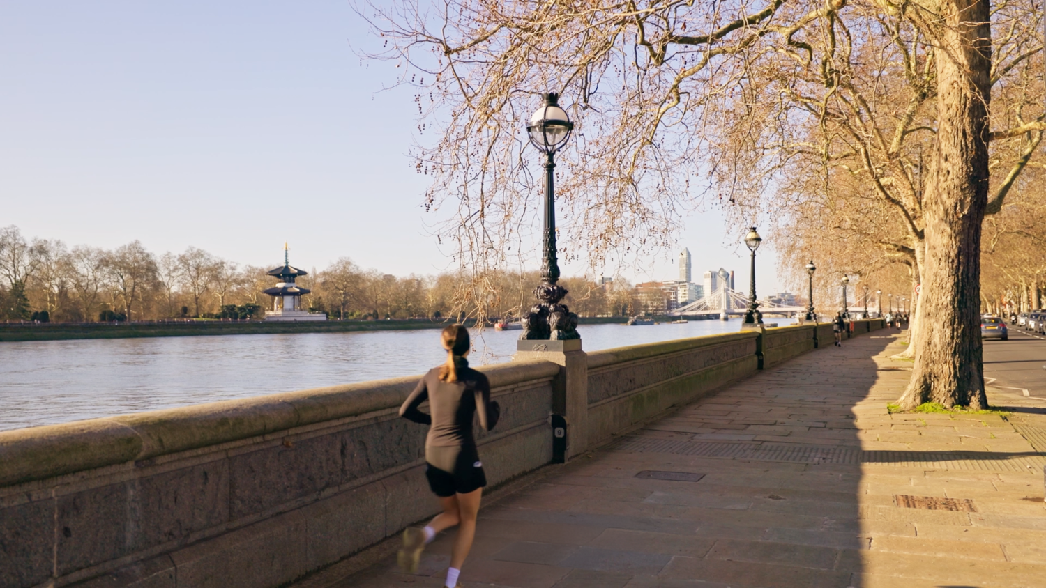 Lady running alongside the River Thames on Chelsea Embankment, with the pagoda at Battersea Park in the distance across the river